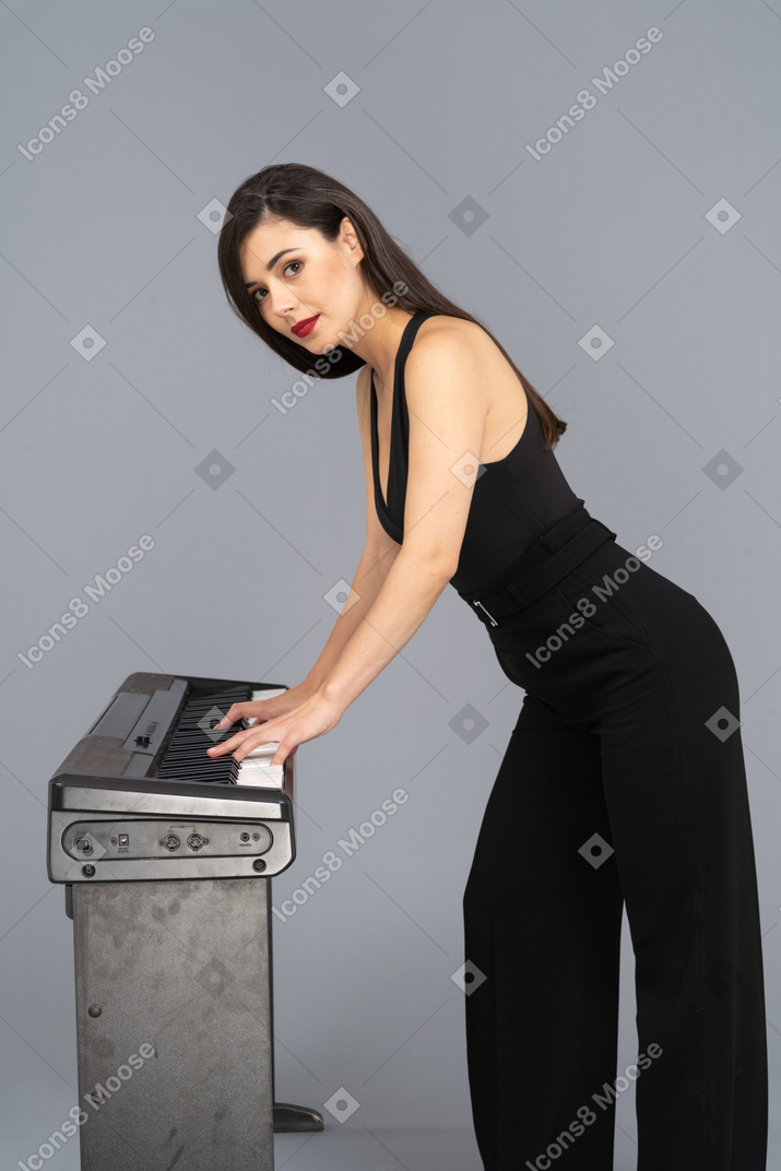 カメラを見ながらピアノを弾く黒いスーツを着た若い女性の側面図