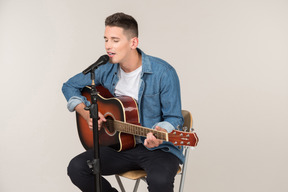 Young guy sitting on the table in profile and playing on guitar