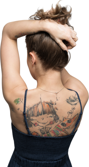 Женщина стоит спиной к камере и поднимает волосы, чтобы показать татуированную спину