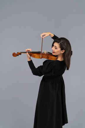 Close-up de uma jovem alegre de vestido preto tocando violino