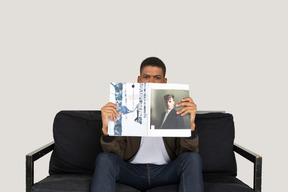 Vista frontal del joven sentado en un sofá y sosteniendo una revista