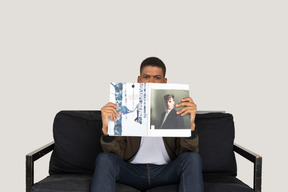 Front view of young man sitting on a sofa and holding a magazine