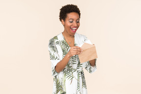 Black short-haired woman in a white and green dress, standing with an envelope in her hand