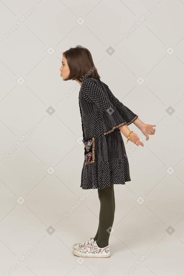 Vista lateral de uma menina em um vestido estendendo as mãos e inclinando-se para a frente