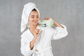 Smiling woman in bathrobe opening a sheet mask pack