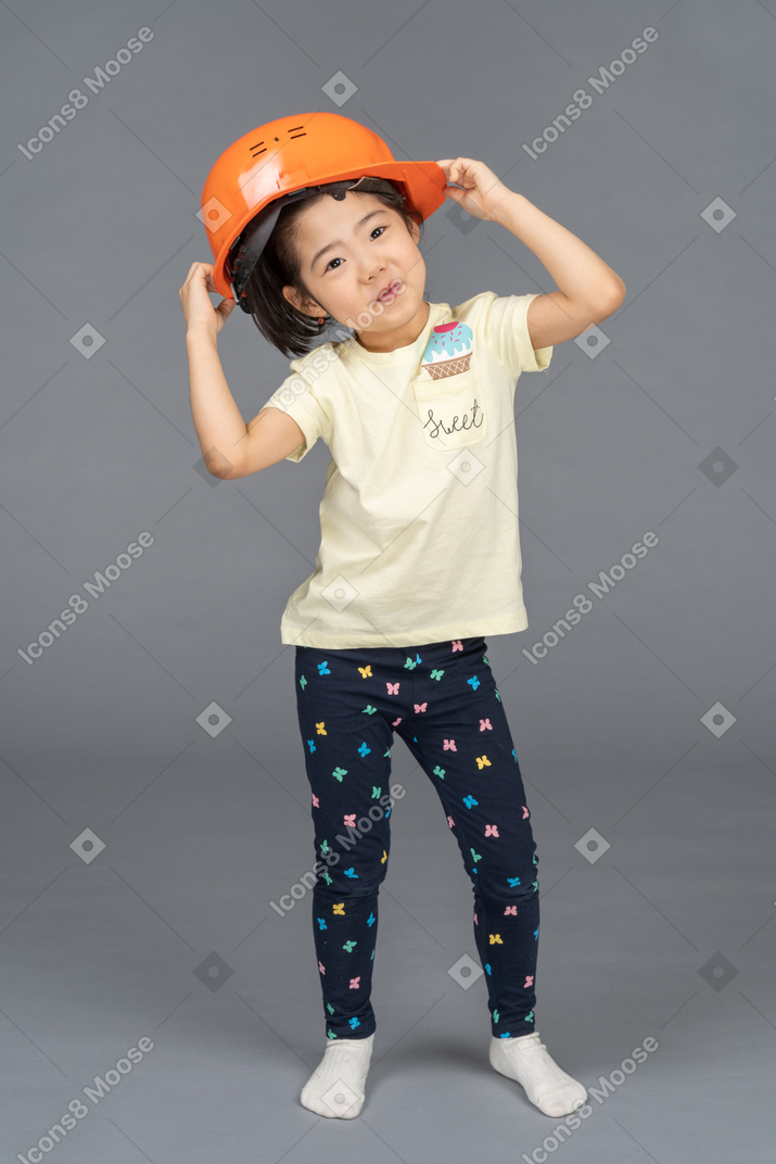 Kleines mädchen posiert beim aufsetzen eines orangefarbenen schutzhelms