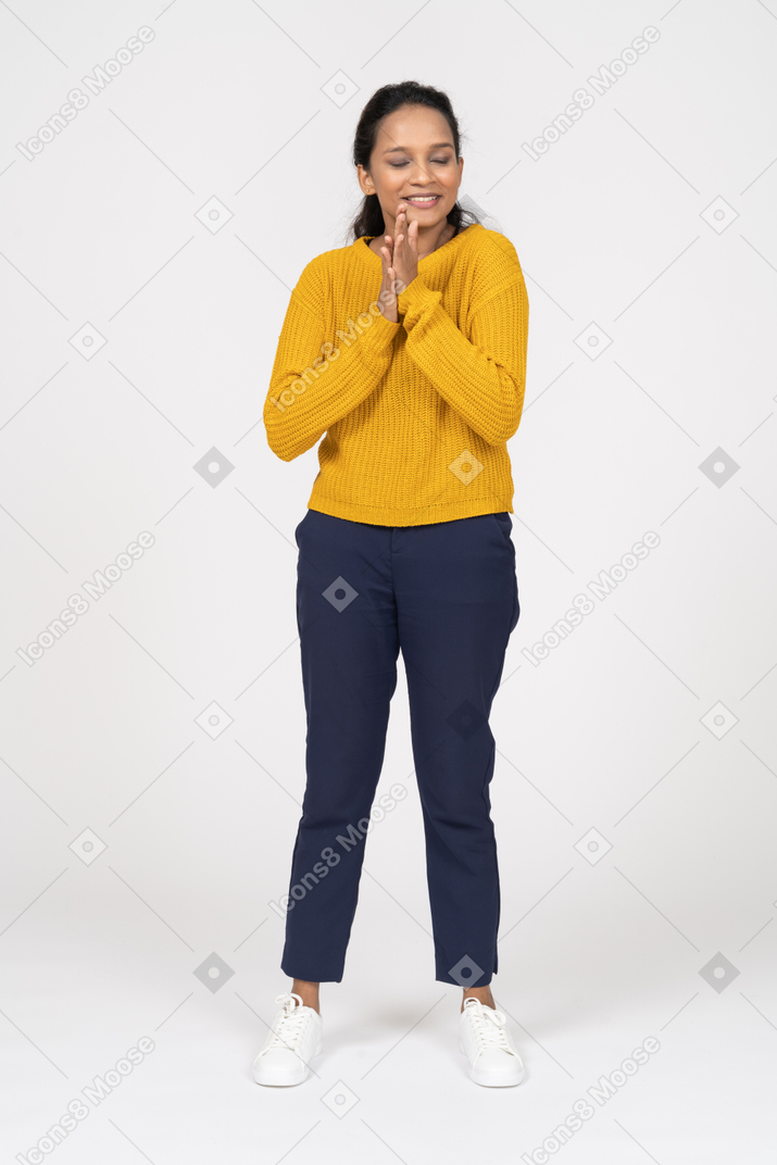 Front view of a cute girl in casual clothes standing with closed eyes and rubbing hands