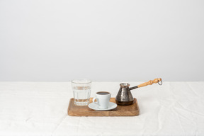 Cezve, vaso de agua y taza de café en la bandeja de madera.