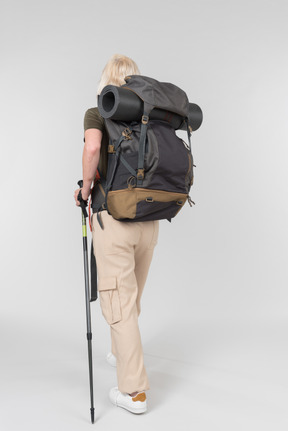 Female tourist carrying backpack and walking with sticks back to camera