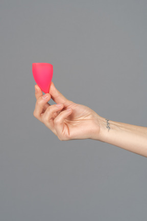 Close up of a hand holding menstrual cup over gray background