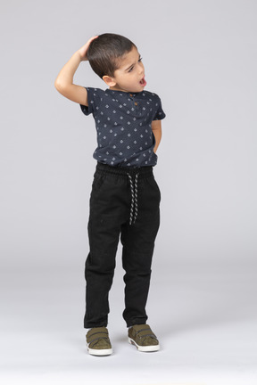 Vista frontal de um menino com roupas casuais em pé com a mão atrás da cabeça