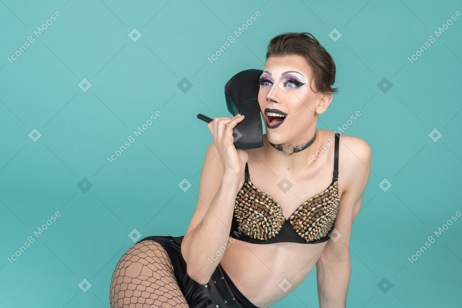 Drag queen in studded bra using shoe as phone