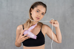 Front view of a young woman wrapping a hairdryer cord around her neck