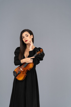 Vista frontal de uma jovem de vestido preto segurando o violino