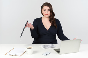 Confuso jovem plus-size feminino trabalhador de escritório, sentado à mesa