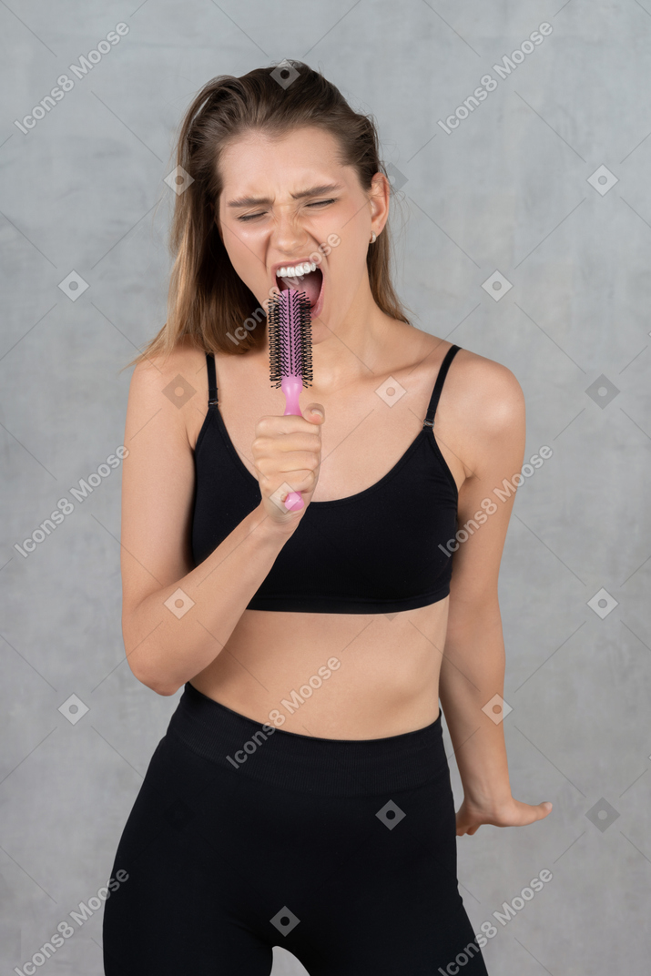 Ritratto di una giovane donna che dà una performance emotiva e usa la spazzola per capelli come microfono