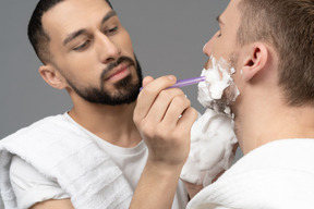 Nahaufnahme eines jungen mannes, der das gesicht seines partners rasiert