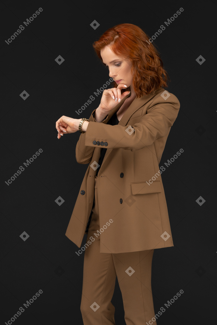 Standing half sideways young woman in formal suit looking at wristwatch