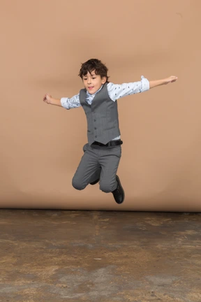 Front view of a cute boy in suit jumping with outstretched arms