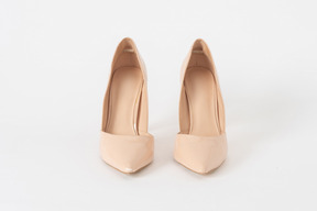 A front shot of a pair of beige lacquered stiletto shoes