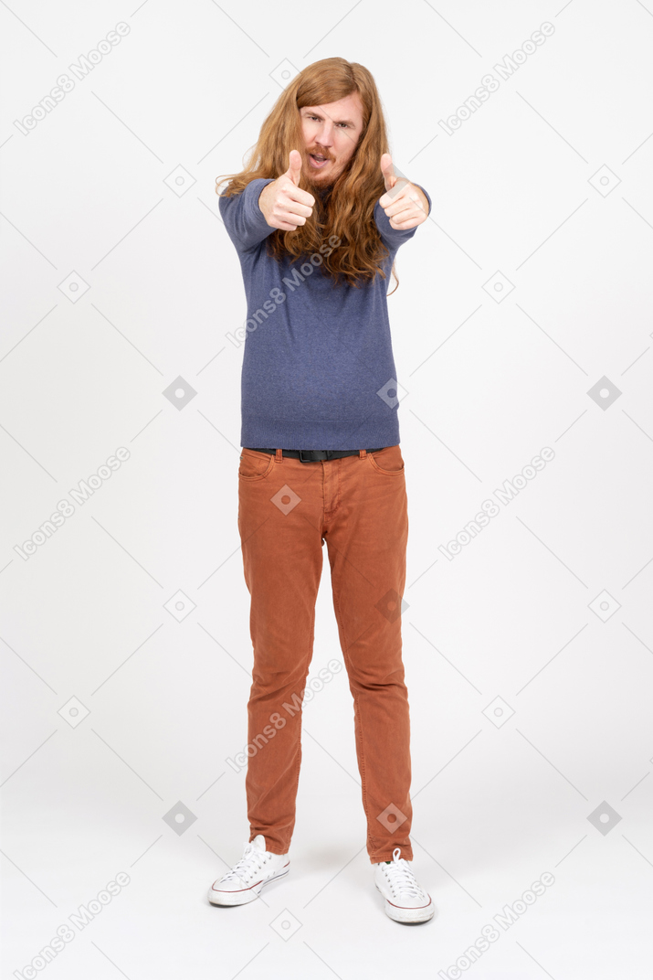 Вид спереди на молодого человека в повседневной одежде, показывающего большие пальцы вверх и смотрящего в камеру