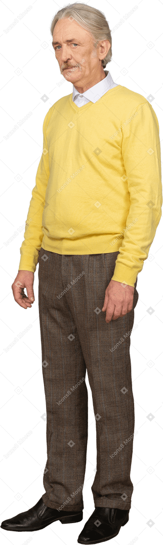 Vue de trois quarts d'un vieil homme mécontent portant un pull jaune et regardant la caméra