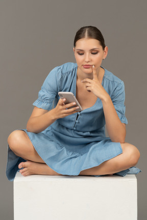 Front view of young woman sitting on a cube and phone messaging