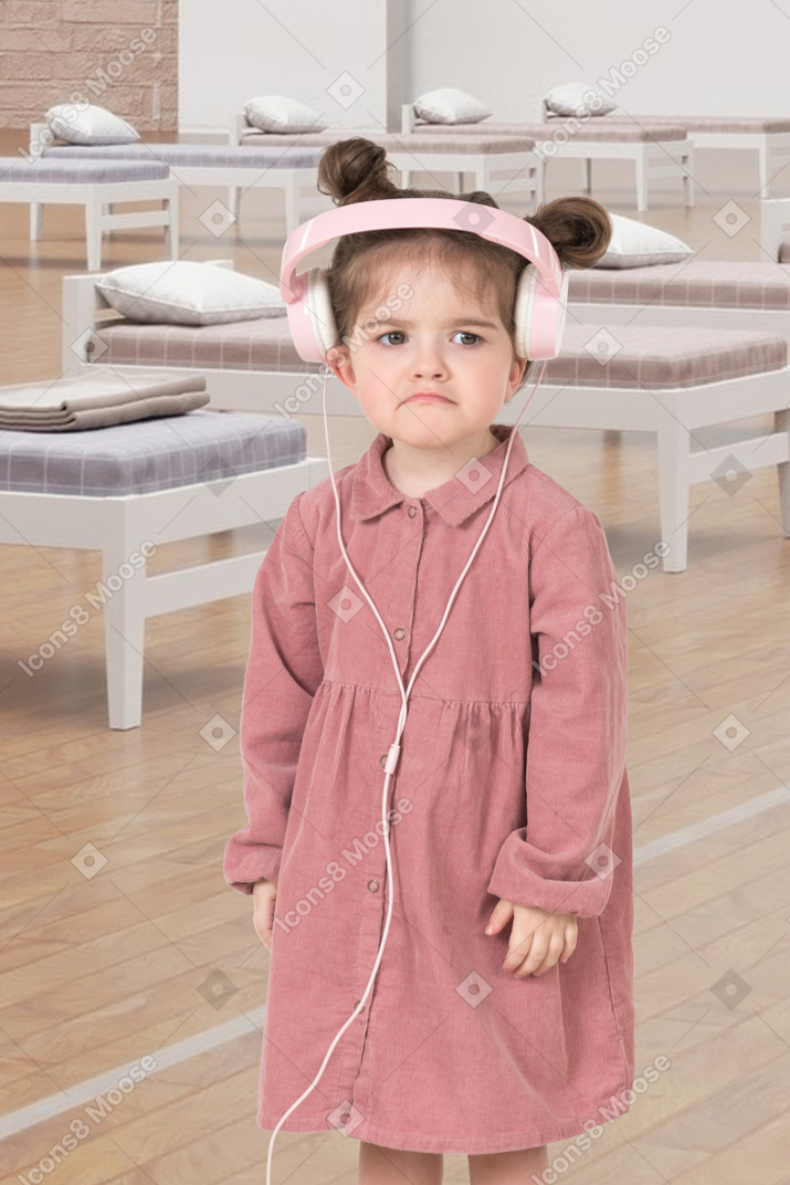 A little girl wearing a pink dress and headphones