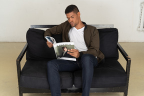 Beautiful young man sitting on a sofa and holding a magazine