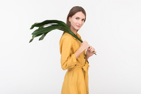 Mujer joven de pie de perfil y sosteniendo una rama verde en su hombro