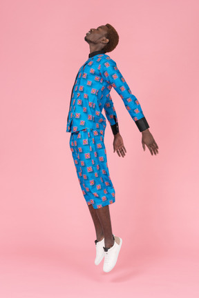 Black man in blue pajamas jumping on pink background