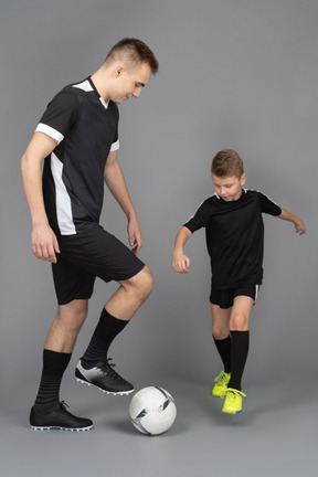 De cuerpo entero de un joven entrenando a un niño pequeño cómo jugar fooyball