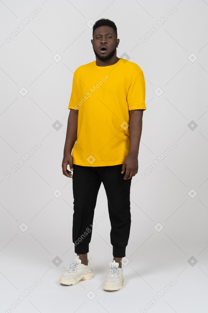 Vista frontal de un asombrado joven de piel oscura con camiseta amarilla parado