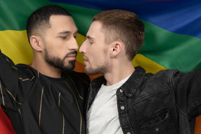 Gros plan de deux jeunes hommes tenant un drapeau lgbt et touchant sensuellement le nez