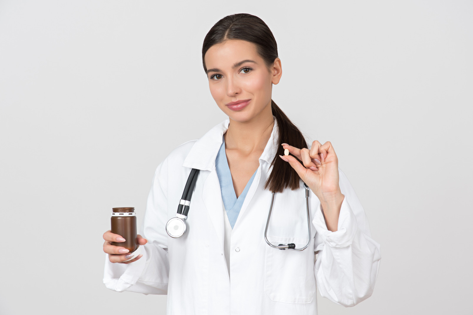 Young female doctor holding pills bottle and one pill