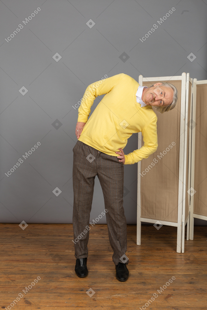 Front view of an old man putting hands on hips while leaning aside