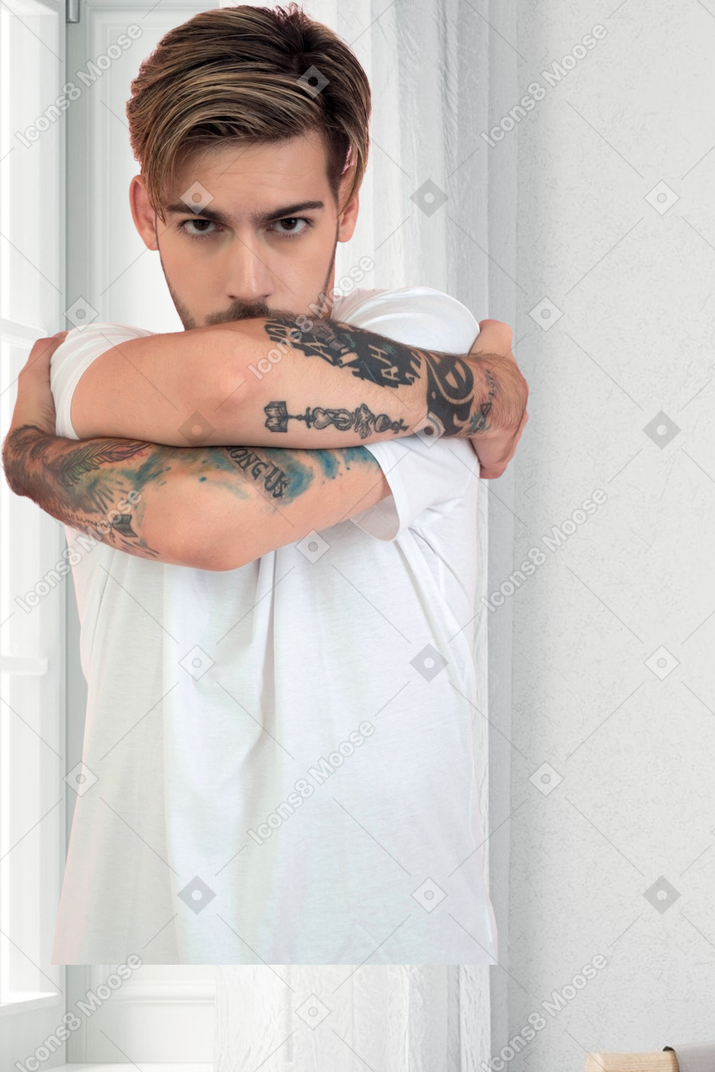 A man with tattoos hugging himself