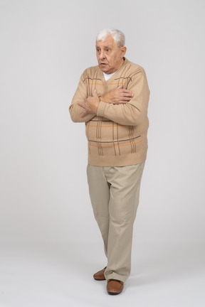 Front view of a scared old man in casual clothes standing with hands on chest