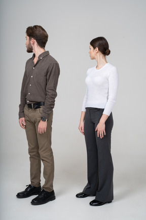 Vista de tres cuartos de una pareja joven en ropa de oficina girando la cabeza
