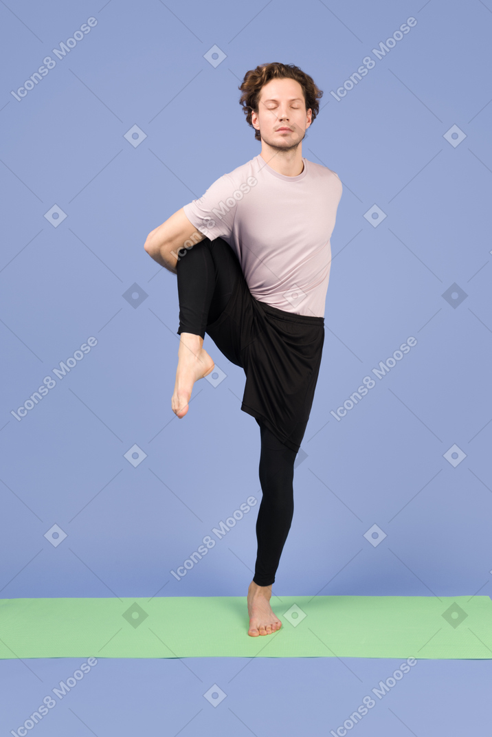 Guy with closed eyes standing on his one leg and holding hands back