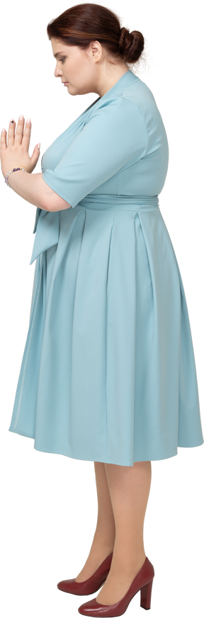祈りのジェスチャーを作る青いドレスを着た女性の側面図