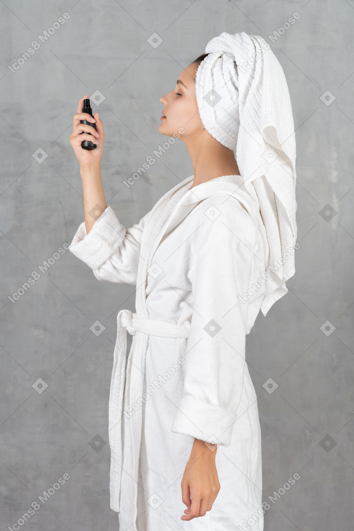 Side view of a woman in bathrobe spraying her face