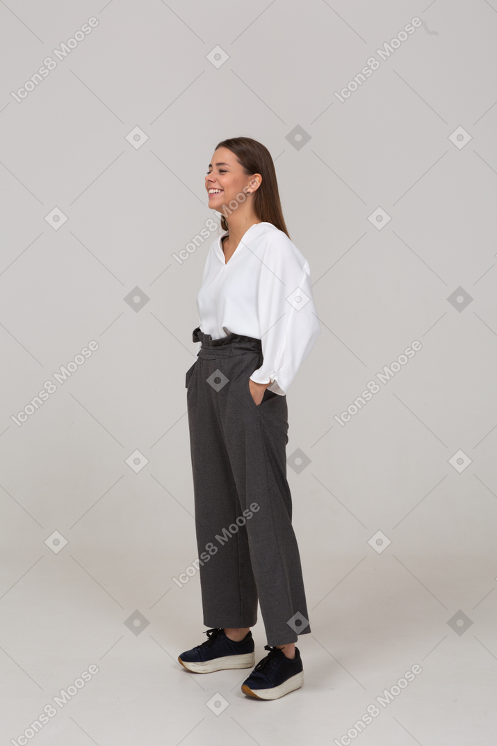 Vue de trois quarts d'une jeune femme souriante en vêtements de bureau mettant les mains dans les poches