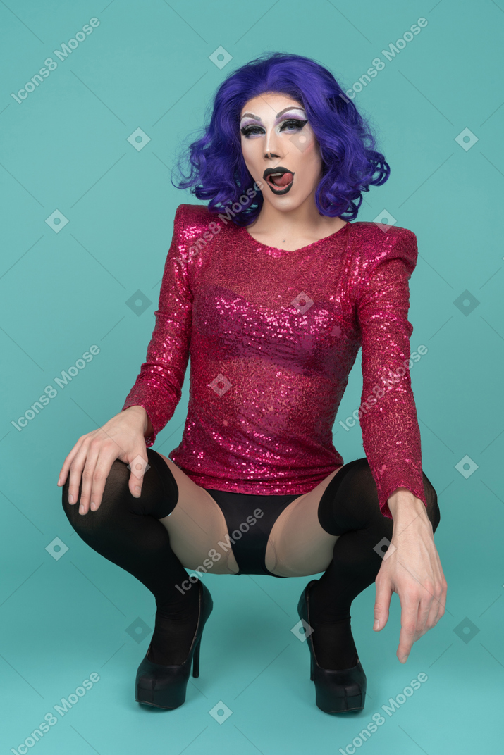 Portrait of a drag queen licking lips while squatting