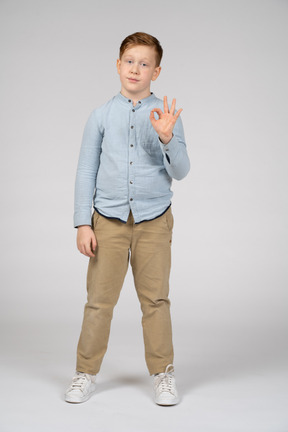 Vista frontal de um menino mostrando sinal de ok e olhando para a câmera