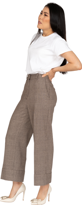 Vista di tre quarti di una giovane donna in calzoni e maglietta che si tocca la schiena