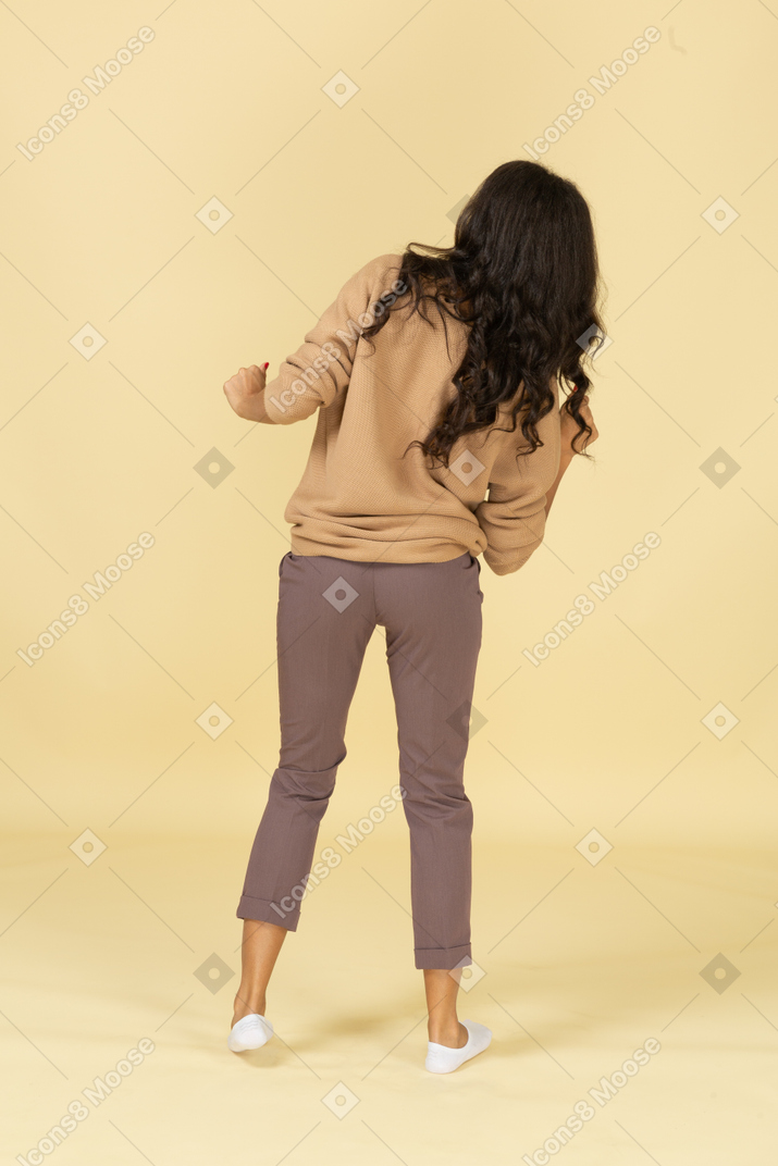 Back view of a dancing dark-skinned young female raising hands