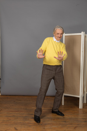 Front view of a shy smiling old man outstretching his hands