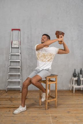 Three-quarter view of a man on a stool swinging an ukulele angrily