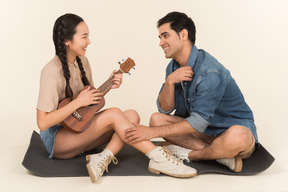 Young asian woman playing her guitar and young man is enchanted by her